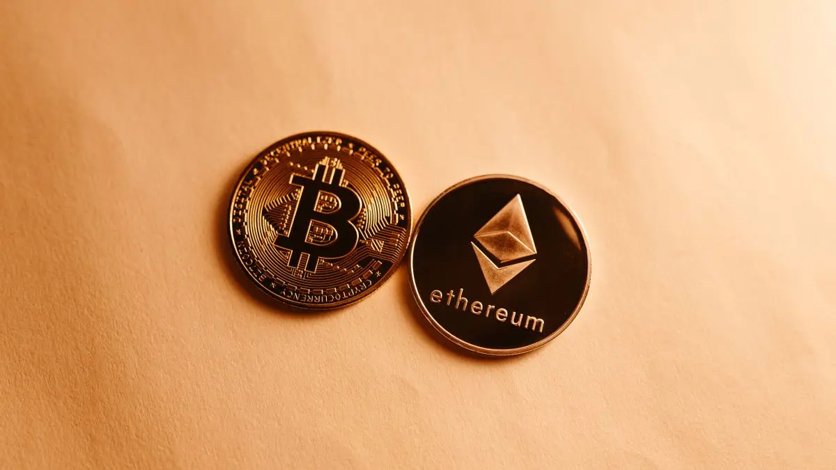 Bitcoin and Ethereum souvenir coins on a peach background.