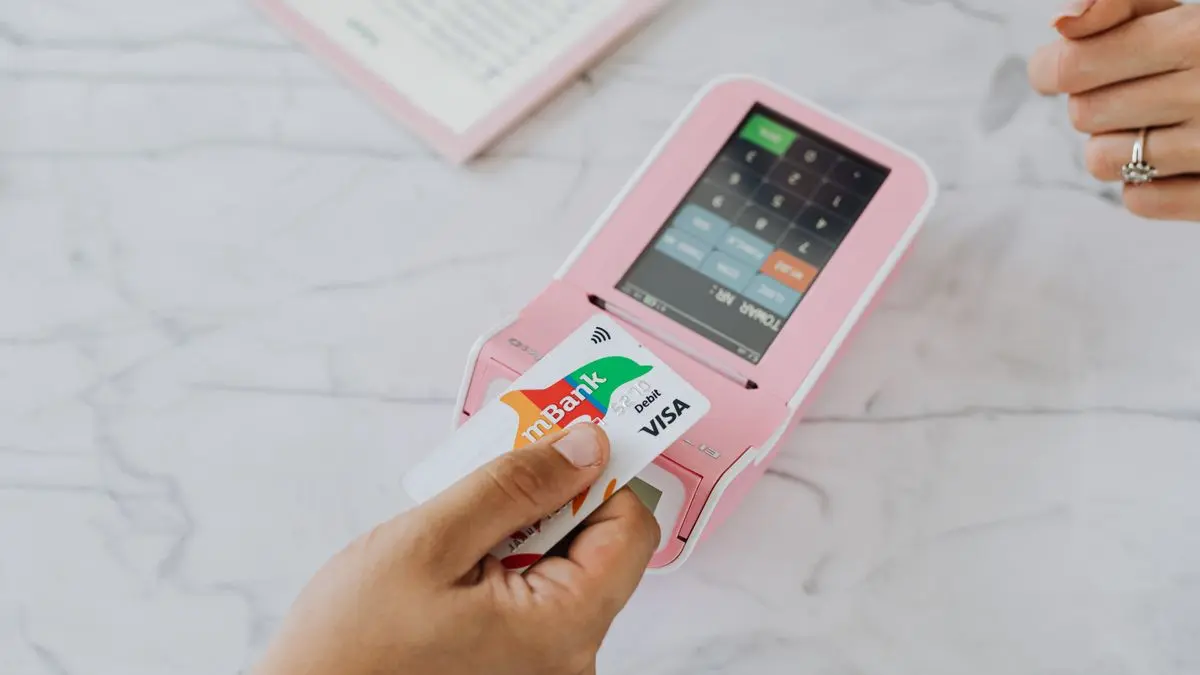 A payment card held beside a pink payment terminal.