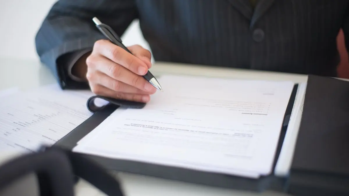A hand signs a document with a pen.