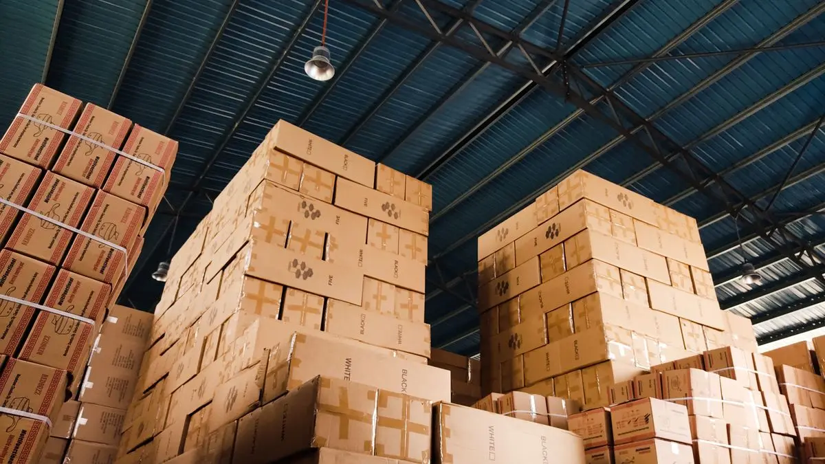 Cardboard boxes stacked beneath a warehouse roof.
