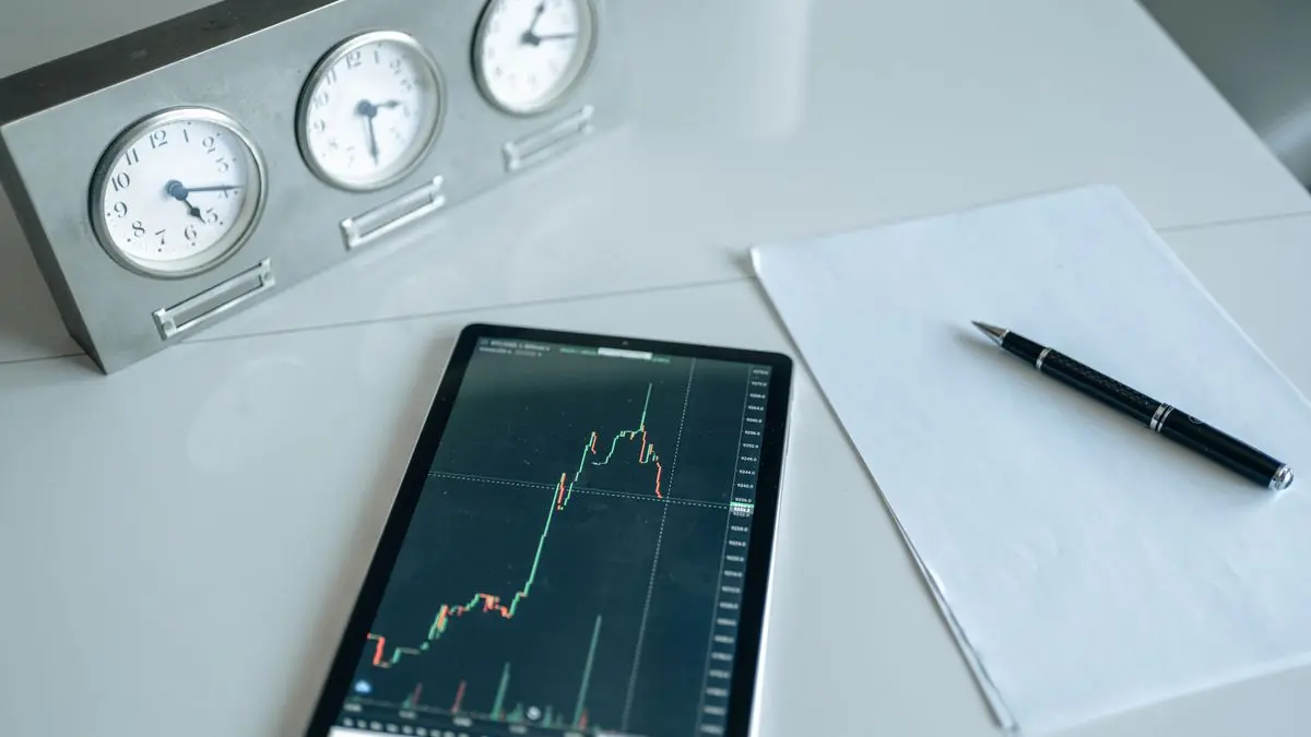 Tablet showing a market chart beside clocks and a notebook.