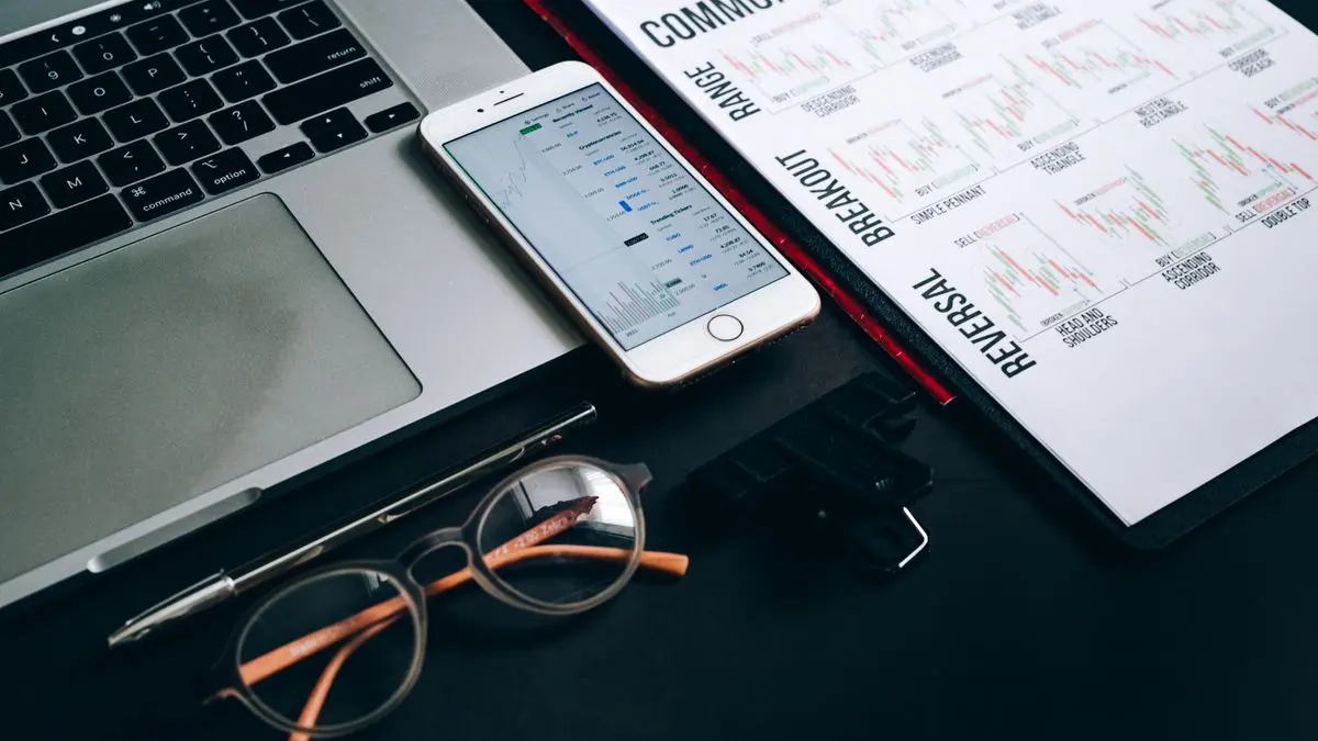 Laptop, phone and printed market charts on a desk.